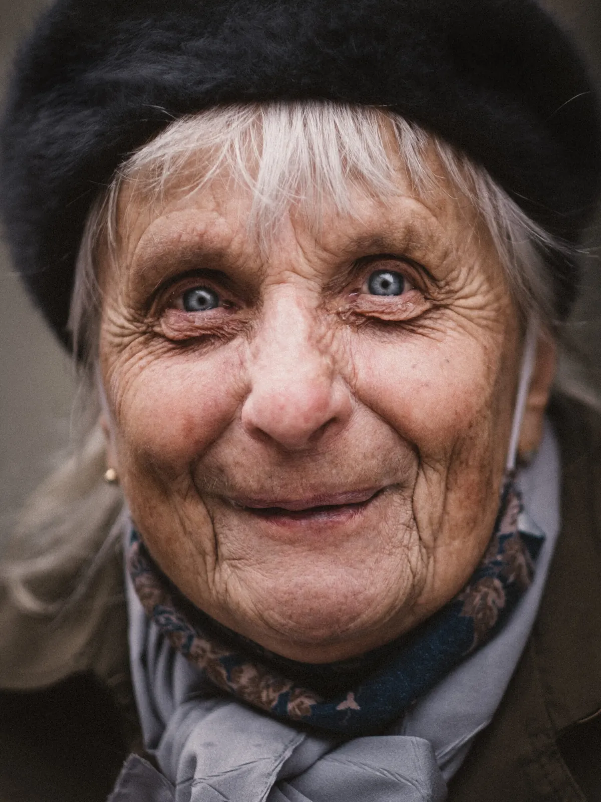 Strassenporträt einer älteren Frau mit Mütze und hellblauen Augen, die herzlich lächelt